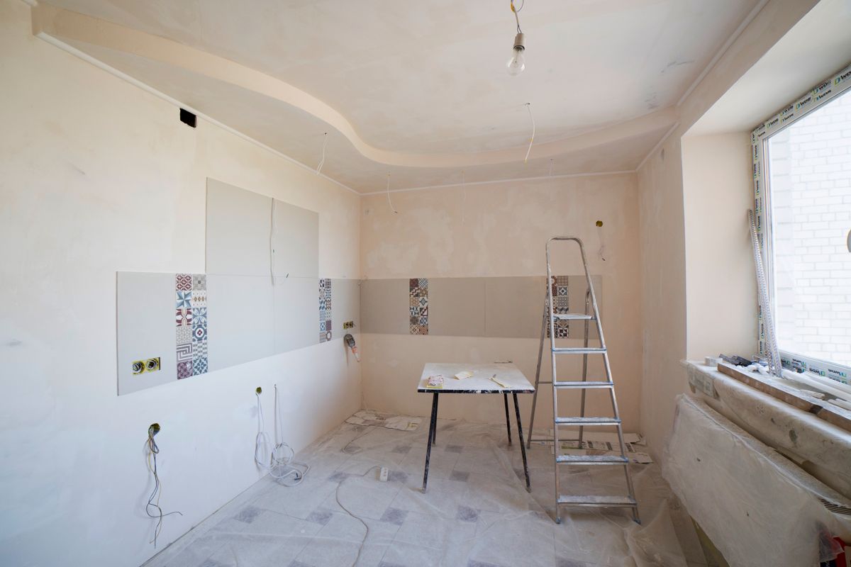 Cucina in ristrutturazione con rivestimento a mosaico parzialmente posato e scala a libretto