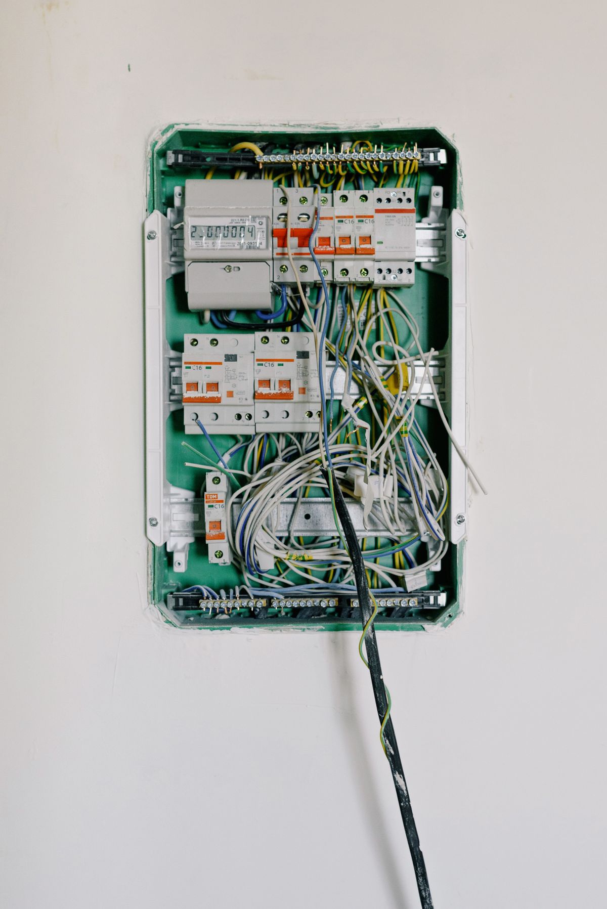 Quadro elettrico aperto a muro con interruttori magnetotermici e cavi in fase di collegamento